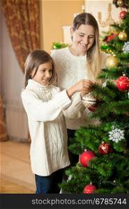 Cute girl helping mother to decorate Christmas tree at living room