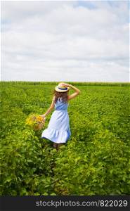 Cute girl in a hat stands in a green field with a bouquet of wild flowers.. Cute girl in a hat stands in a green field with a bouquet of wild flowers