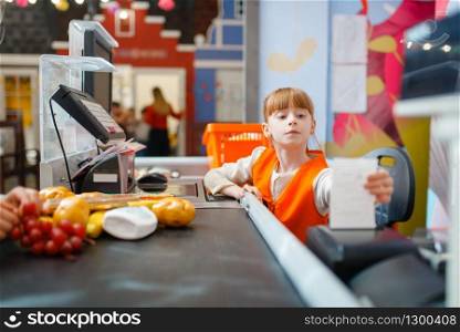 Cute girl in uniform at the cash register makes a check for the purchase, saleswoman, playroom. Kids plays sellers in imaginary supermarket, salesman profession learning