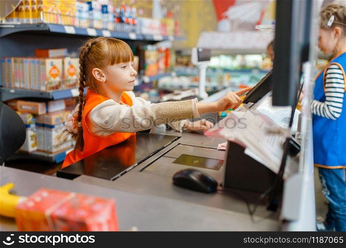 Cute girl in uniform at the cash register playing saleswoman, playroom. Kids plays sellers in imaginary supermarket, salesman profession learning. Girl in uniform at the cash register, playroom