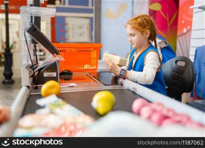 Cute girl in uniform at the register playing saleswoman, playroom. Kids plays sellers in imaginary supermarket, salesman profession learning