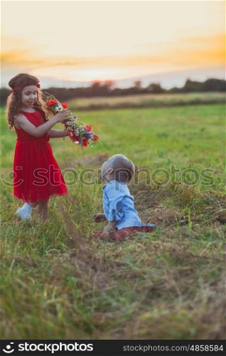 Cute girl is trying to put a floral wreath on her brother head. Brother and sister