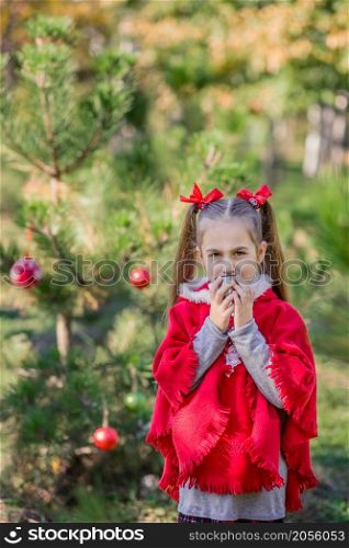 Cute girl is warmed by a cup of tea on a cold day on the background of the Christmas tree. Merry Christmas and happy holidays.. Cute girl is warmed by a cup of tea on a cold day on the background of the Christmas tree