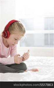 Cute girl listening music on smart phone in bedroom