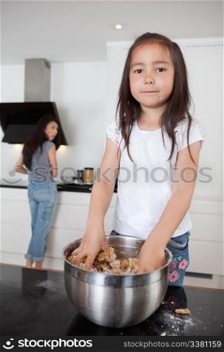 Cute girl mixing dough in kitchen with mother in background