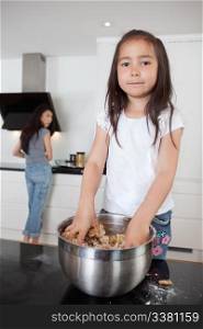 Cute girl mixing dough in kitchen with mother in background