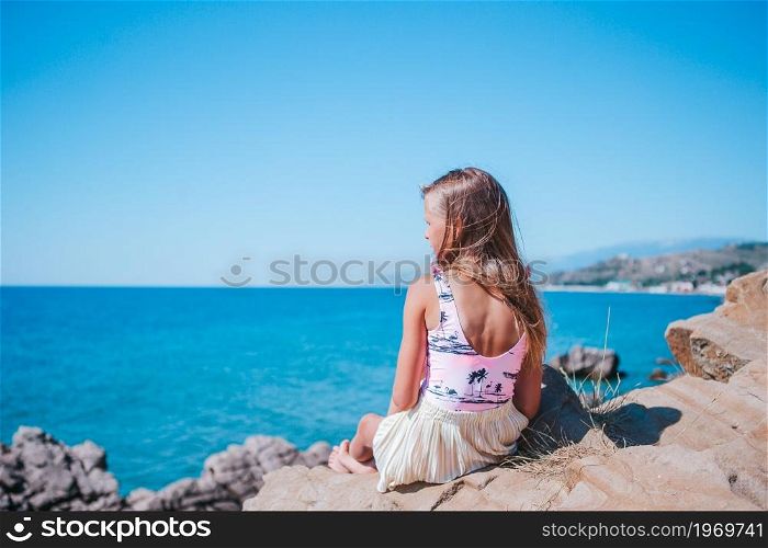 Cute girl on edge of cliff seashore enjoy the view on mountain top rock. Little girl outdoor on edge of cliff seashore