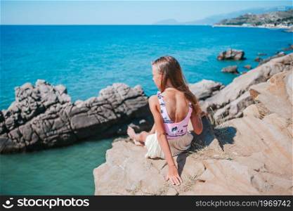 Cute girl on edge of cliff seashore enjoy the view on mountain top rock. Little girl outdoor on edge of cliff seashore