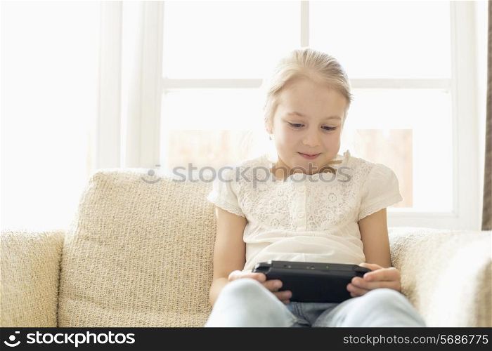 Cute girl playing hand-held video game at home