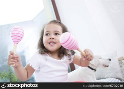 Cute girl playing with maracas while sitting beside dog at home