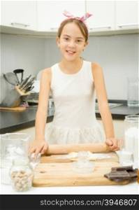 Cute girl rolling dough with wooden pin on kitchen