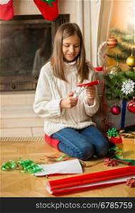 Cute girl sitting at Christmas tree and cutting snowflakes out of decorative paper