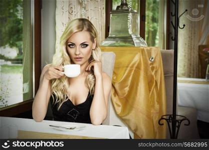cute girl sitting at table in old fashion bar , looking in camera in act to drink a cup of tea