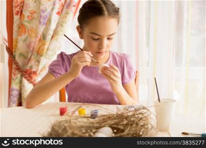 Cute girl sitting on kitchen and painting Easter egg