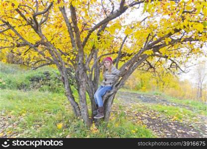 Cute girl sitting on spreading tree in autumn