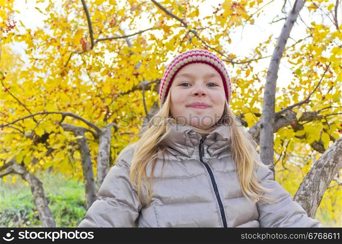 Cute girl sitting on spreading tree in autumn