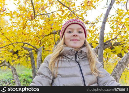 Cute girl sitting on spreading tree in autumn