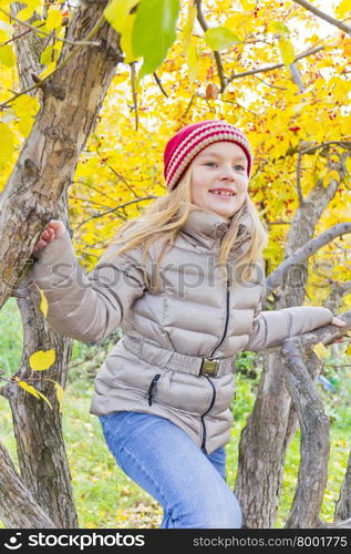 Cute girl sitting on spreading tree in autumn