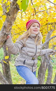 Cute girl sitting on spreading tree in autumn