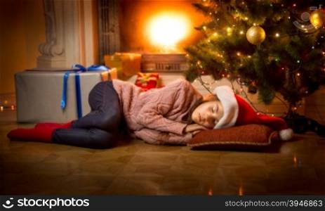 Cute girl sleeping on floor under Christmas tree next to fireplace