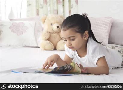 Cute girl turning page while reading book in bed