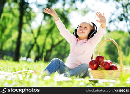 Cute girl wearing headphones sitting in summer park. Sounds of nature