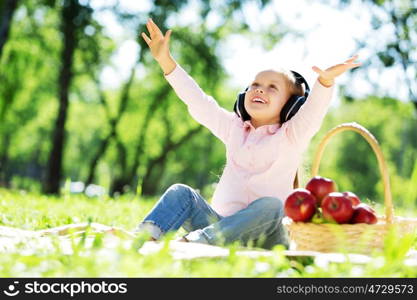 Cute girl wearing headphones sitting in summer park. Sounds of nature