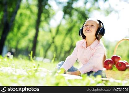 Cute girl wearing headphones sitting in summer park. Sounds of nature