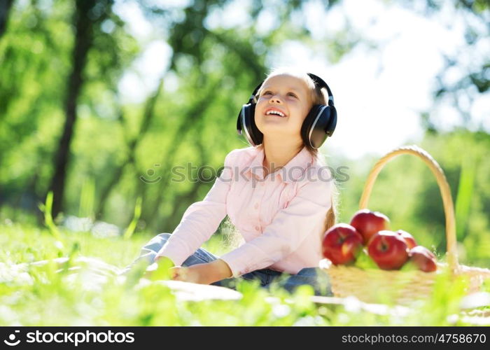 Cute girl wearing headphones sitting in summer park. Sounds of nature