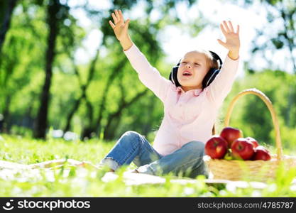 Cute girl wearing headphones sitting in summer park. Sounds of nature