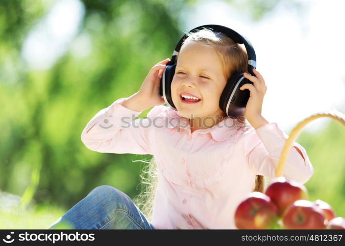 Cute girl wearing headphones sitting in summer park. Sounds of nature