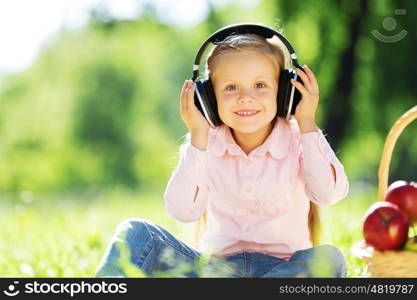 Cute girl wearing headphones sitting in summer park. Sounds of nature