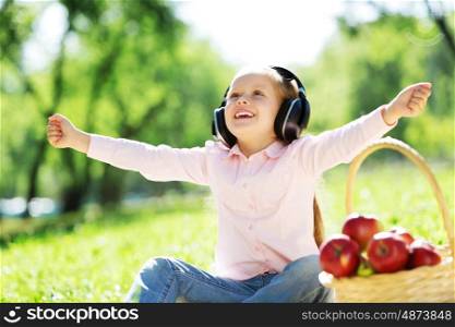 Cute girl wearing headphones sitting in summer park. Sounds of nature