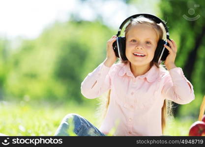 Cute girl wearing headphones sitting in summer park. Sounds of nature