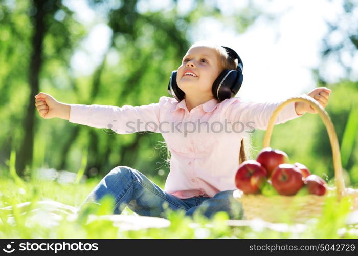 Cute girl wearing headphones sitting in summer park. Sounds of nature