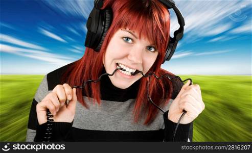 Cute girl with red hair biting the cord of her headphones while listening to music. Studio shot.
