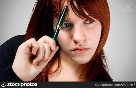 Cute girl with red hair holding a pen against her forehead and thinking. Studio shot.