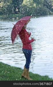 Cute girl with umbrella looking at the river in fall season