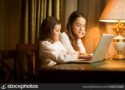 Cute girls sitting at table and using laptop