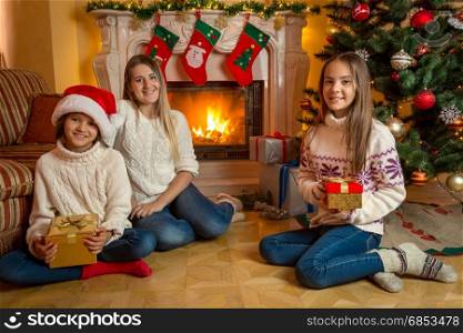 Cute girls with young mother sitting at fireplace in living room decorated for Christmas