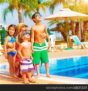 Cute happy family having fun near pool on luxury tropical resort, mother with children looking up in sky, summer holidays, love concept