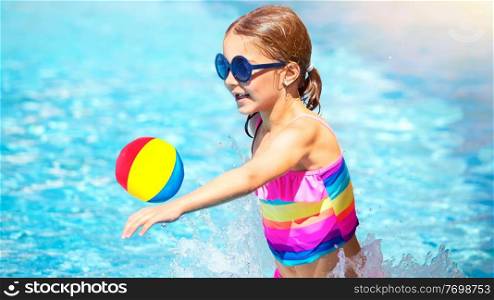 Cute happy little girl playing in the swimming pool with a ball, enjoying summertime activity, spending holidays on the beach resort