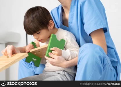 cute kid with disability playing with developing toys while is being helped by physiotherapist in rehabilitation hospital. High quality photo. cute kid with disability playing with developing toys while is being helped by physiotherapist in rehabilitation hospital.