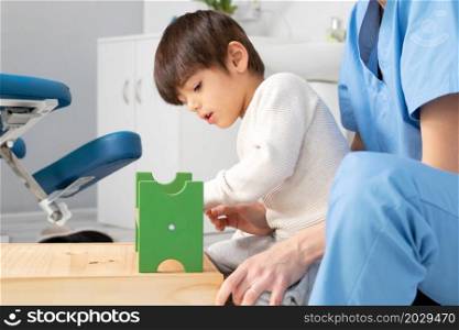 cute kid with disability playing with developing toys while is being helped by physiotherapist in rehabilitation hospital. High quality photo. cute kid with disability playing with developing toys while is being helped by physiotherapist in rehabilitation hospital.