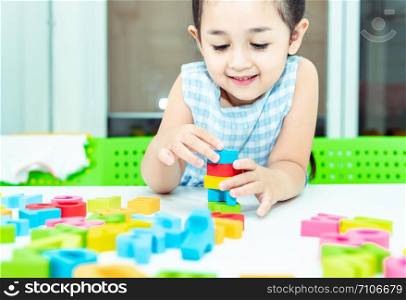 Cute kids female playing with toy designer on the floor at home. Child girl exciting while playing with alphabet colorful blocks. Kindergarten educational games for determination, intention concept