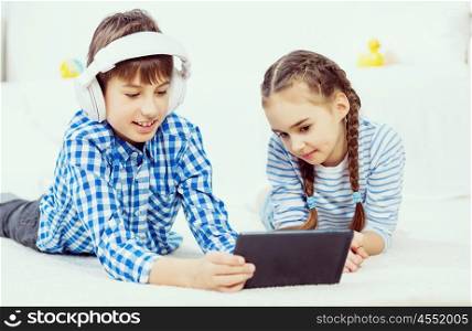 Cute kids gaming on tablet. Boy and girl using tablet while lying on floor