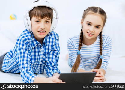 Cute kids gaming on tablet. Boy and girl using tablet while lying on floor