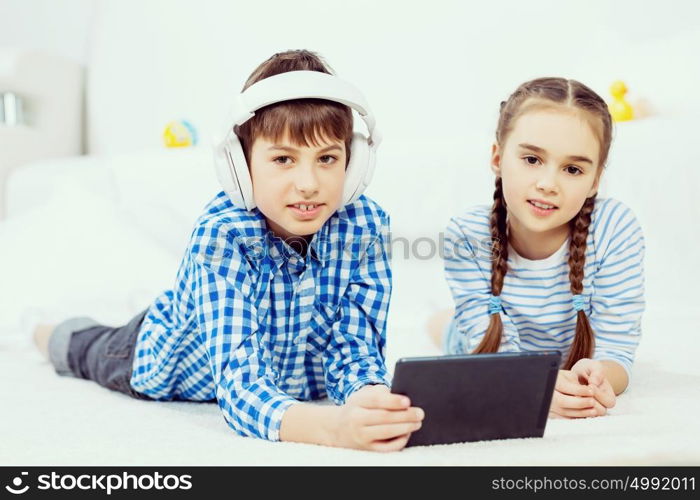 Cute kids gaming on tablet. Boy and girl using tablet while lying on floor