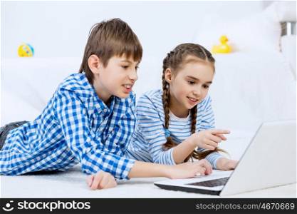 Cute kids using devices . Boy and girl using laptop while lying on floor