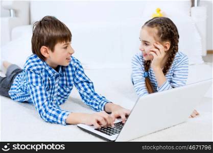 Cute kids using devices . Boy and girl using laptop while lying on floor